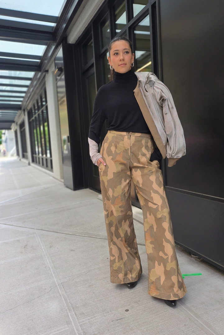 Model styles Carlton Jones camouflage wide-leg pants with a black turtleneck and a jacket over one shoulder